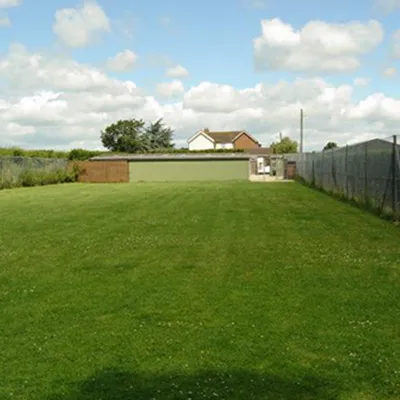 a grassy field with a fence and a house in the background